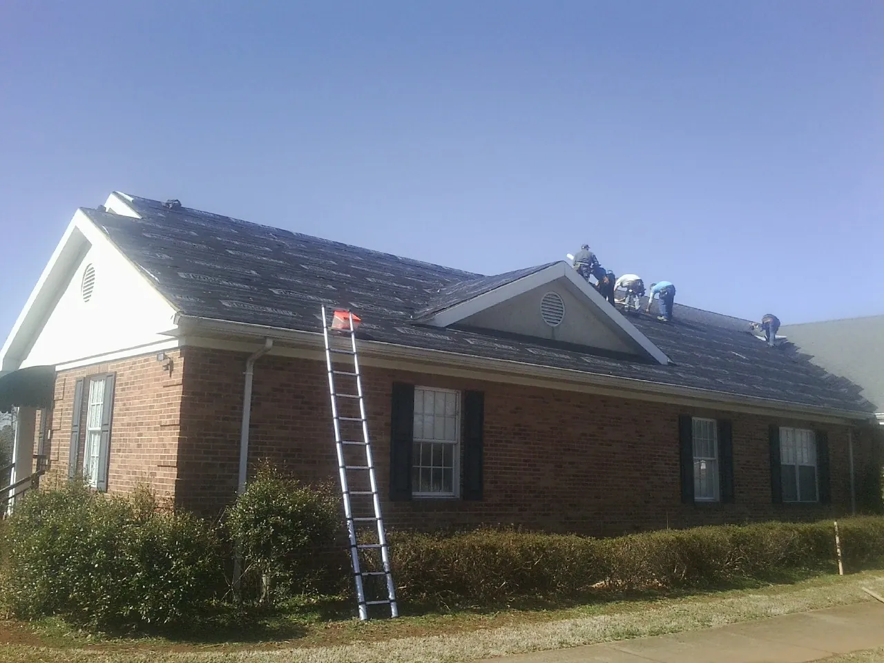 Crew tearing shingles off a brick ranch roof with a ladder set — Emergency Roof Repair work by our crew in Southwick