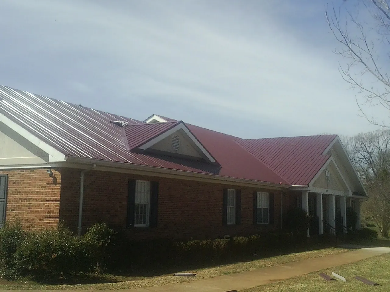 Red metal roof with gabled entries on a long brick building, from a Hail Damage Roof Repair job in Southwick