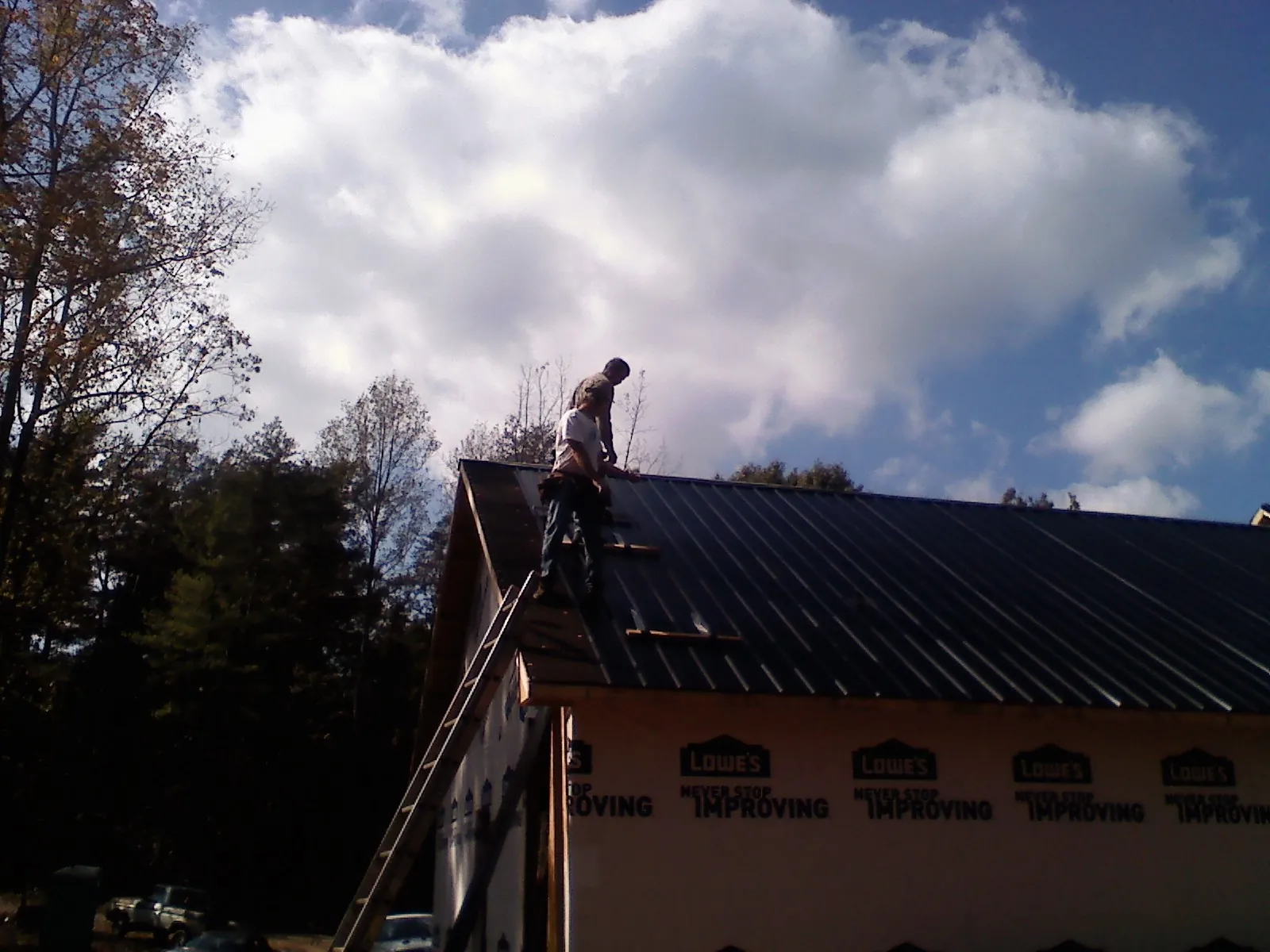Roofer fastening dark metal panels high against a cloudy sky in Southwick