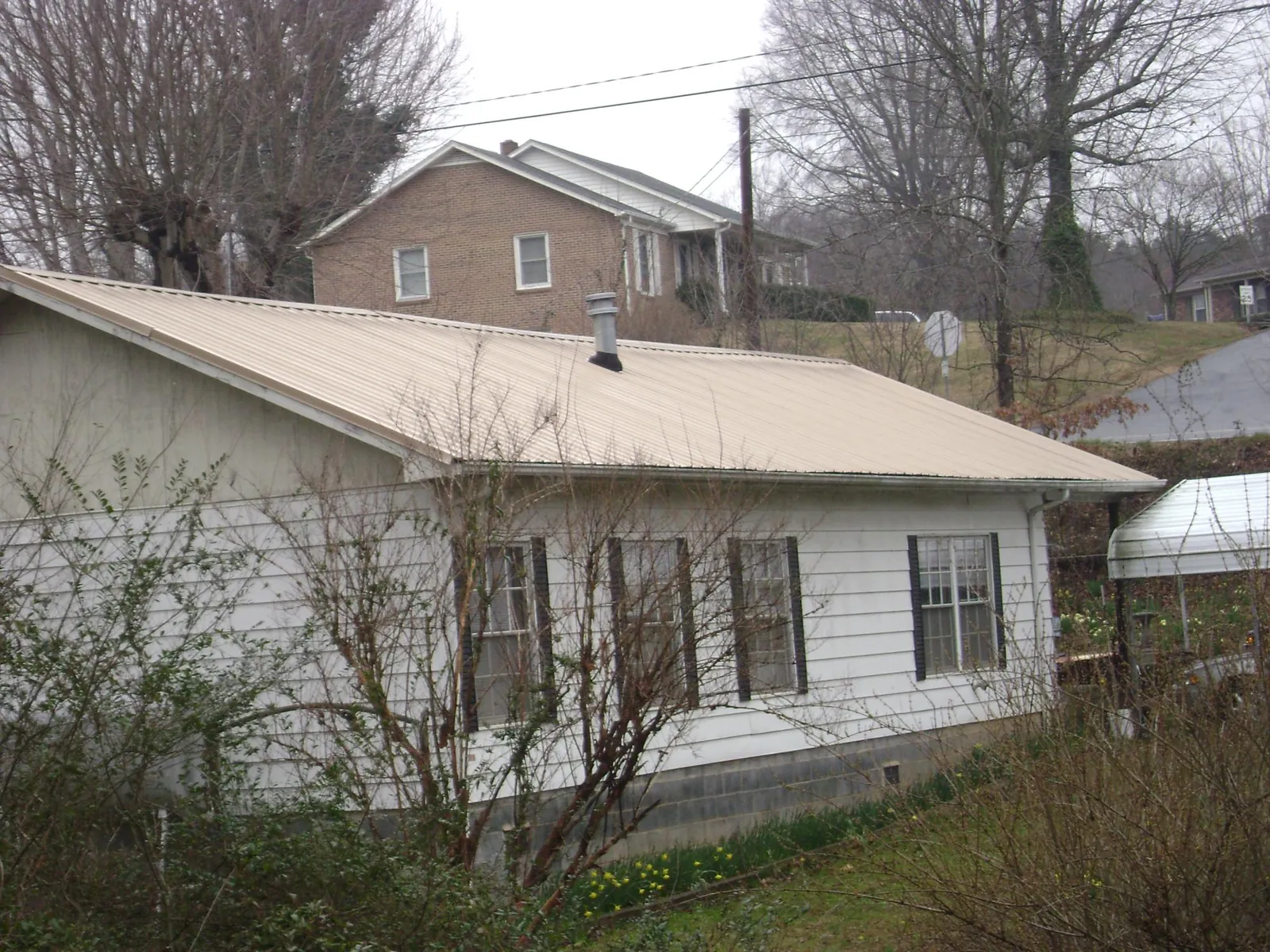Tan metal roof on a white sided house set into a hillside — Commercial Roofing by Roofing Brothers in Southwick